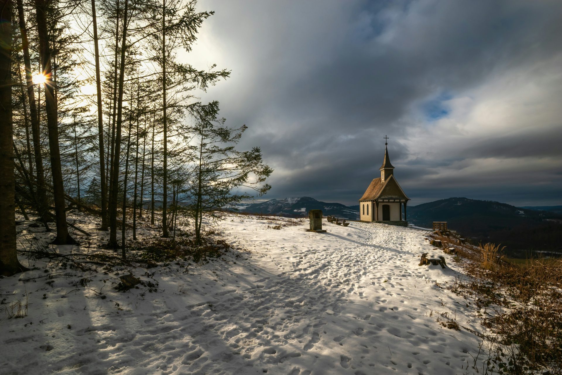 Small chapel on a snowy hill under dramatic clouds